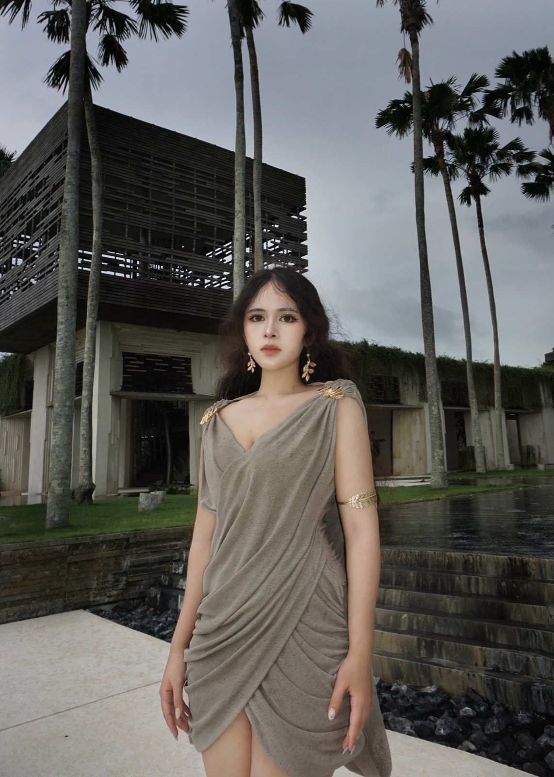 Clara in a draped taupe dress beside a modern building and palm trees