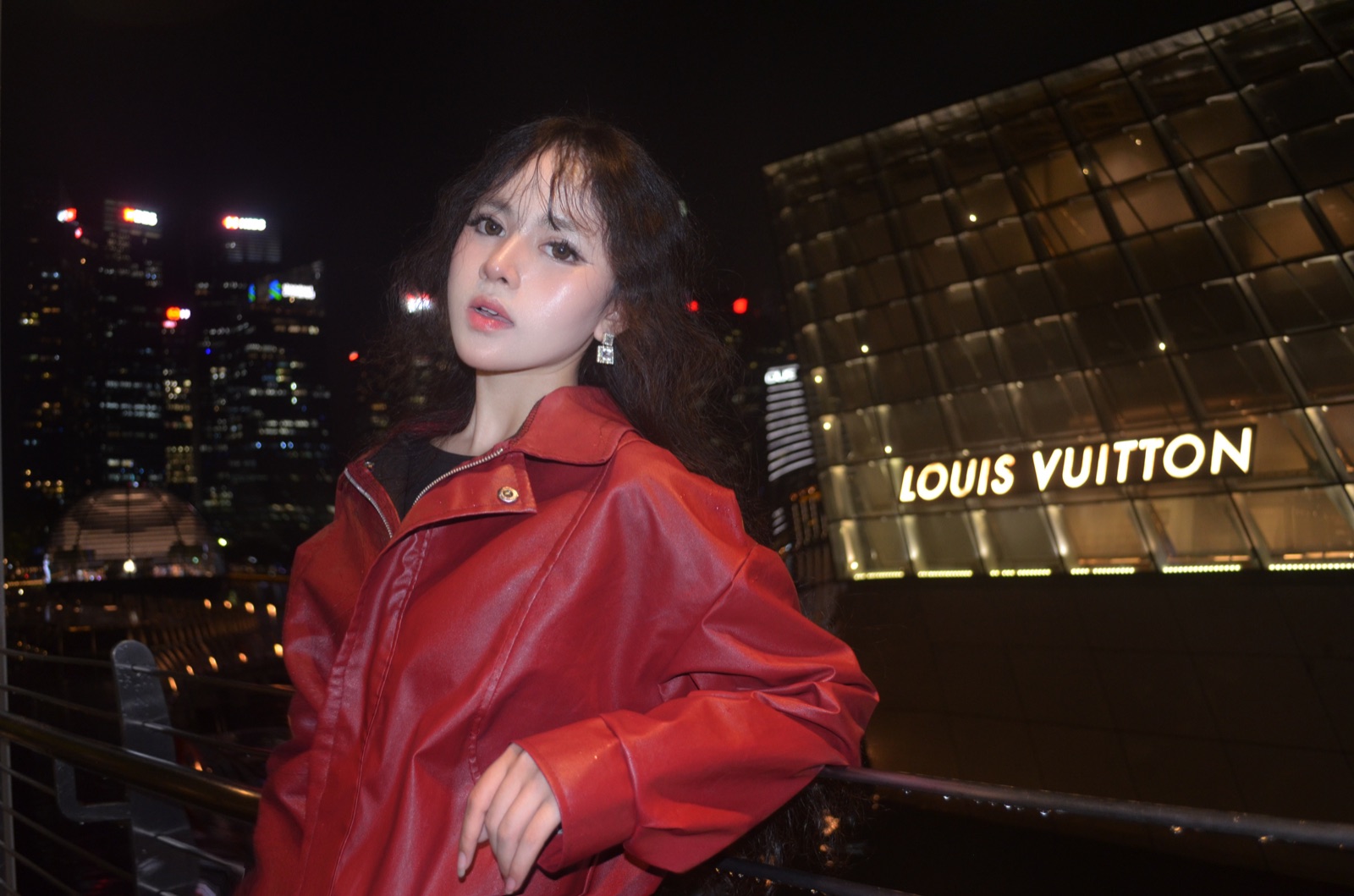 Clara in a red leather jacket in front of Louis Vuitton at night