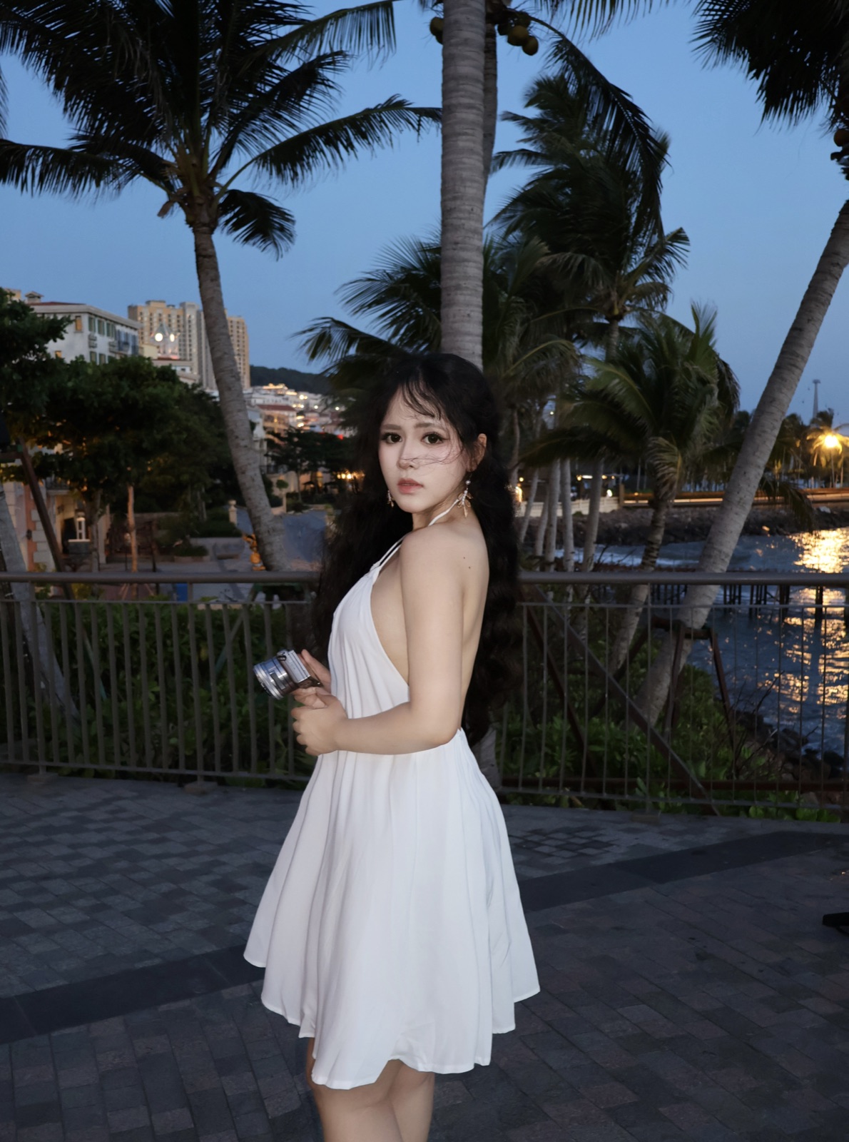 Clara in white beneath palms at dusk