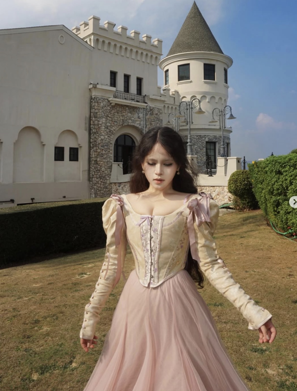 Clara in a pink dress in front of a castle-like villa